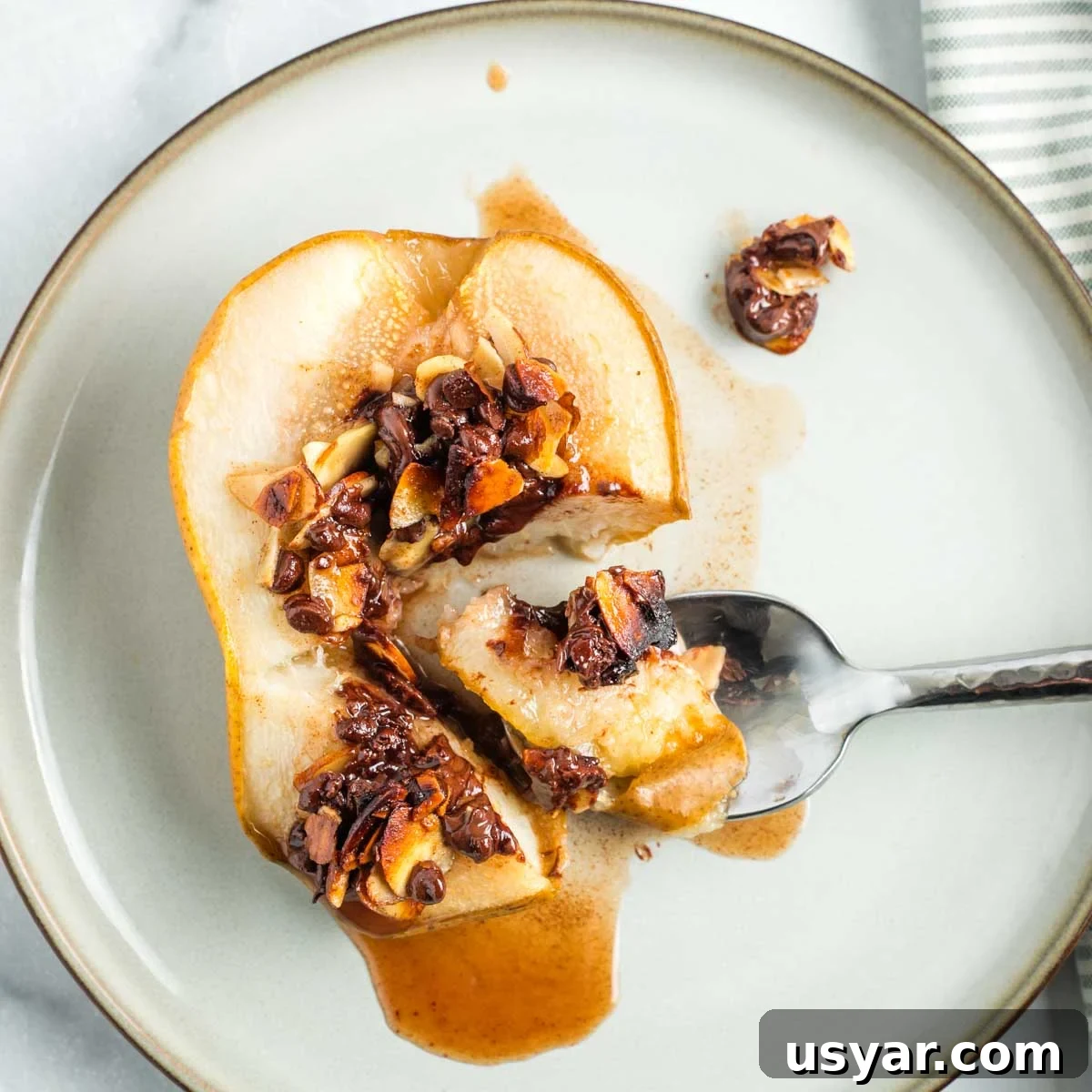 Oven Baked Pears with Almonds and Dark Chocolate 12 Spoonful of baked pear, showing juices oozing out and melty chocolate and golden almonds filled into center cavity.