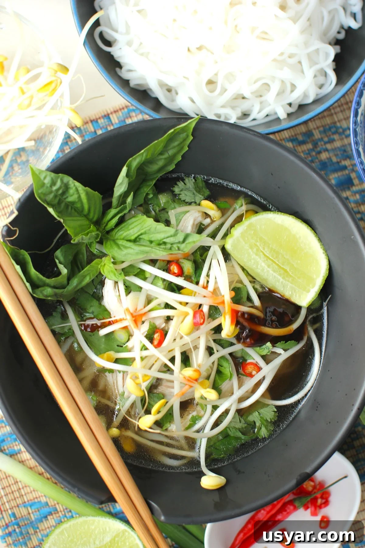 Shortcut Chicken Pho Recipe for Vietnamese Pho Ga 2 a black ceramic bowl of easy chicken pho soup with a bowl of cooked rice noodles beside it.