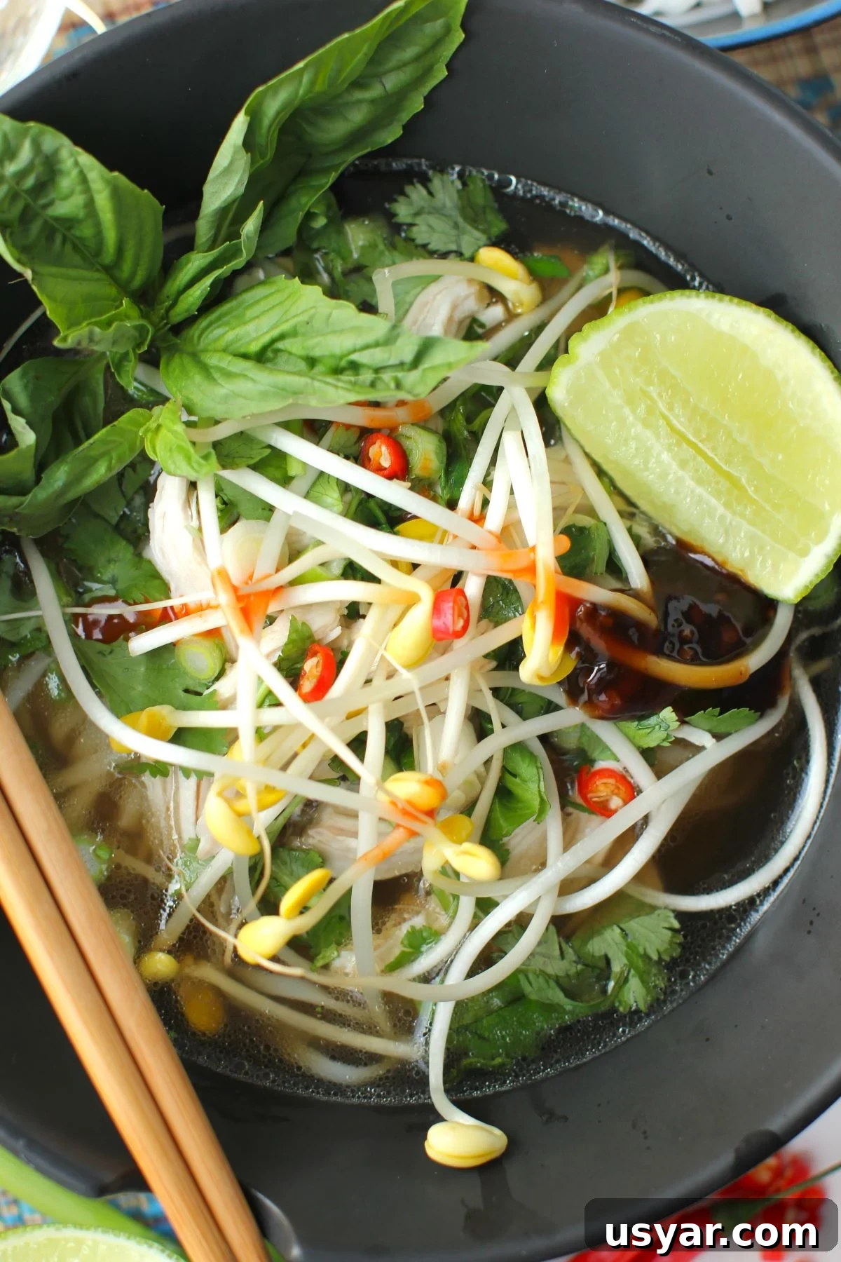 Shortcut Chicken Pho Recipe for Vietnamese Pho Ga 16 pho soup in a black bowl, with lime wedge and basil.