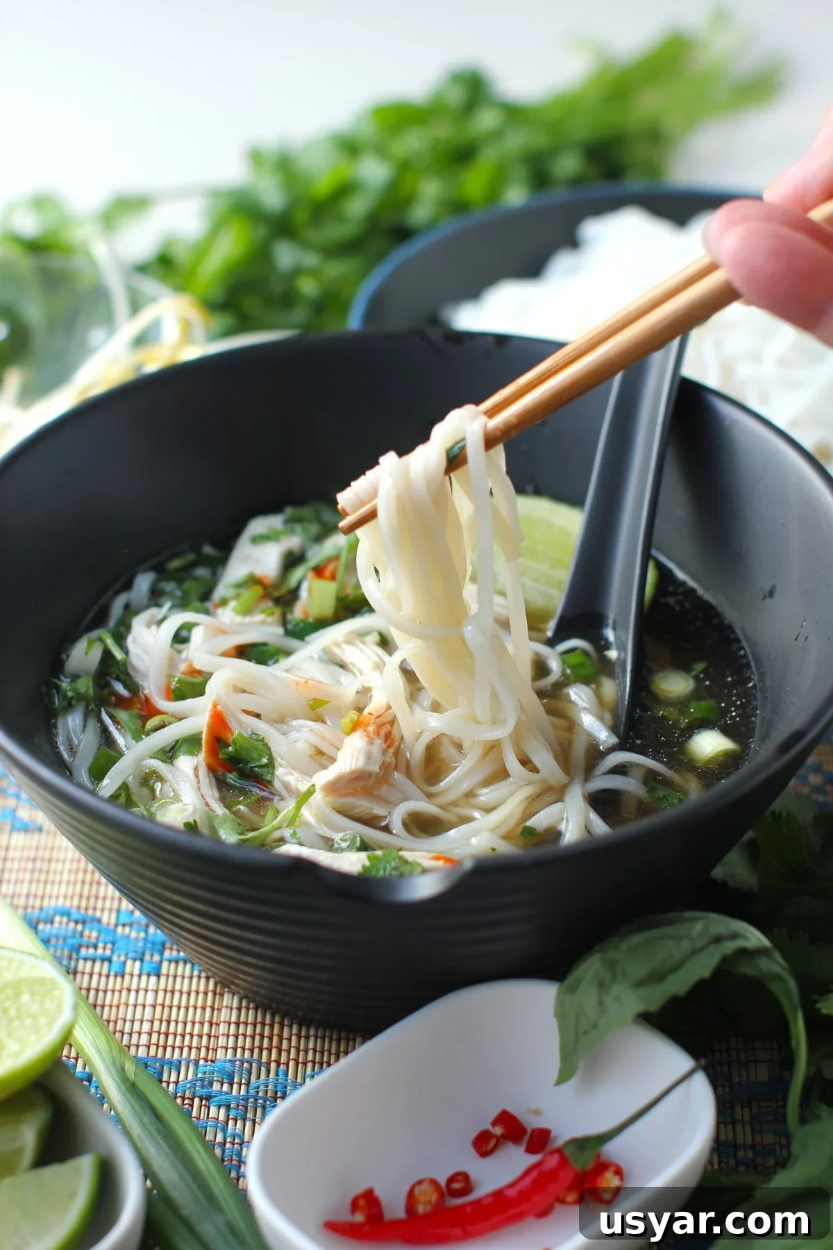 Shortcut Chicken Pho Recipe for Vietnamese Pho Ga 18 lifting the noodles up out of a bowl of pho with chopsticks.