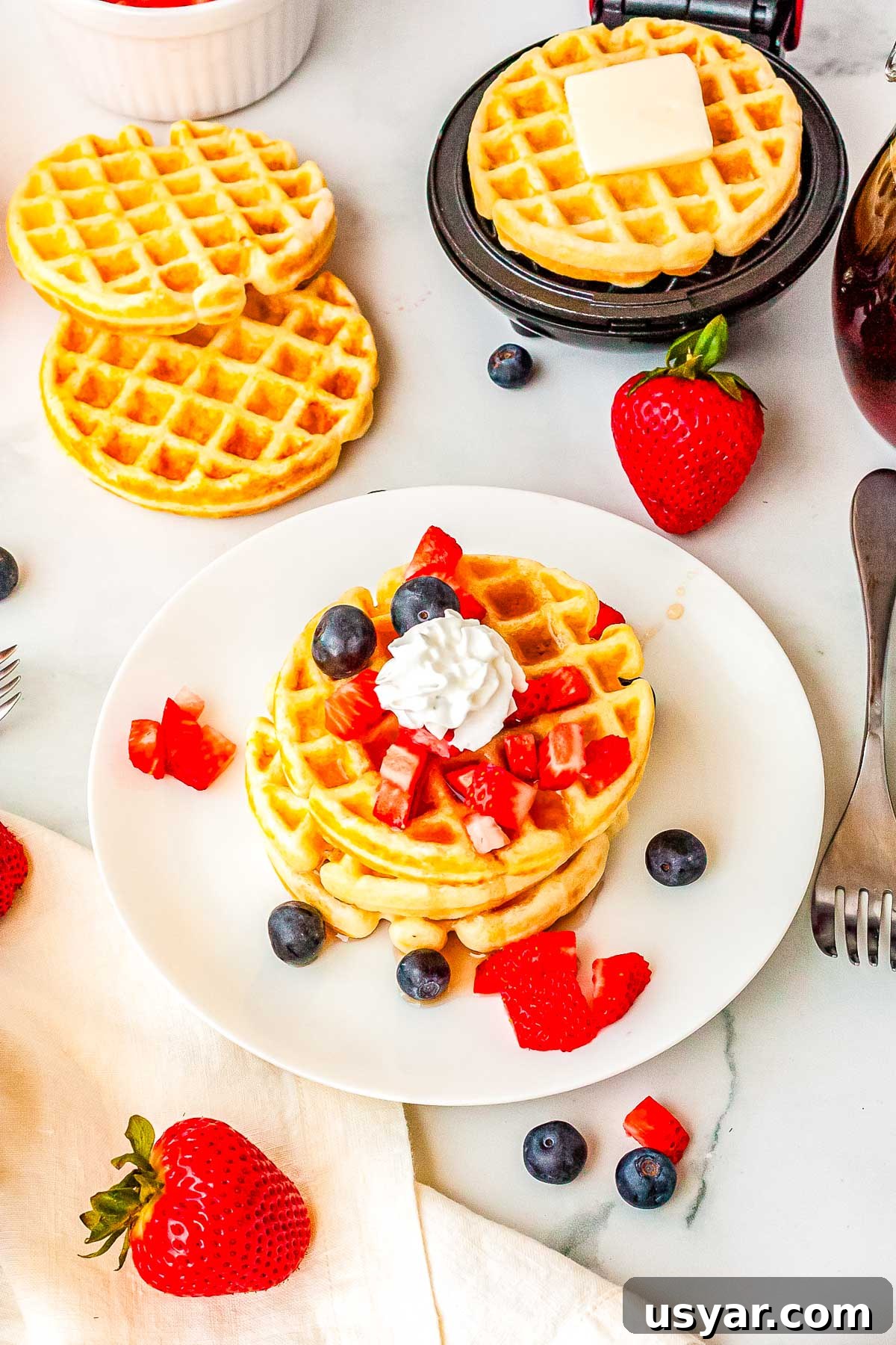 Dash Waffle Maker Recipes for Breakfast, Brunch and Snacks 8 Three waffles on a plate topped with syrup, berries, and whipped cream.