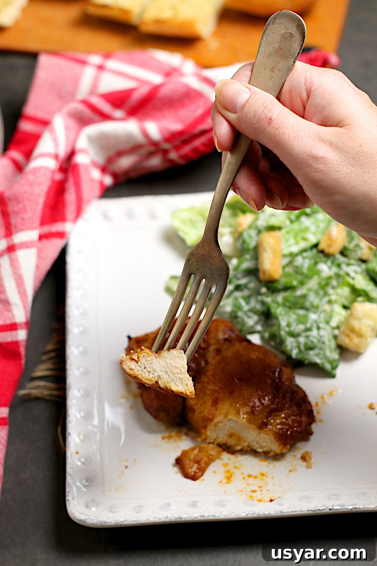 Hot Honey-Glazed Chicken Thighs Recipe 5 A hand holding a fork with a piece of Hot Honey Glazed Chicken Thigh on it.