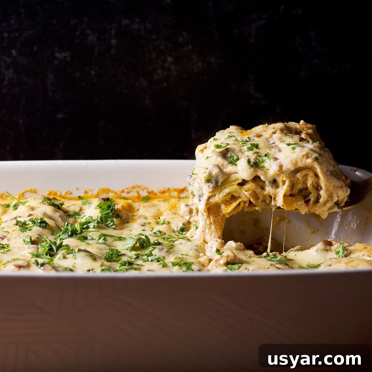 Someone using a spatula to serve a piece of white mushroom lasagna.