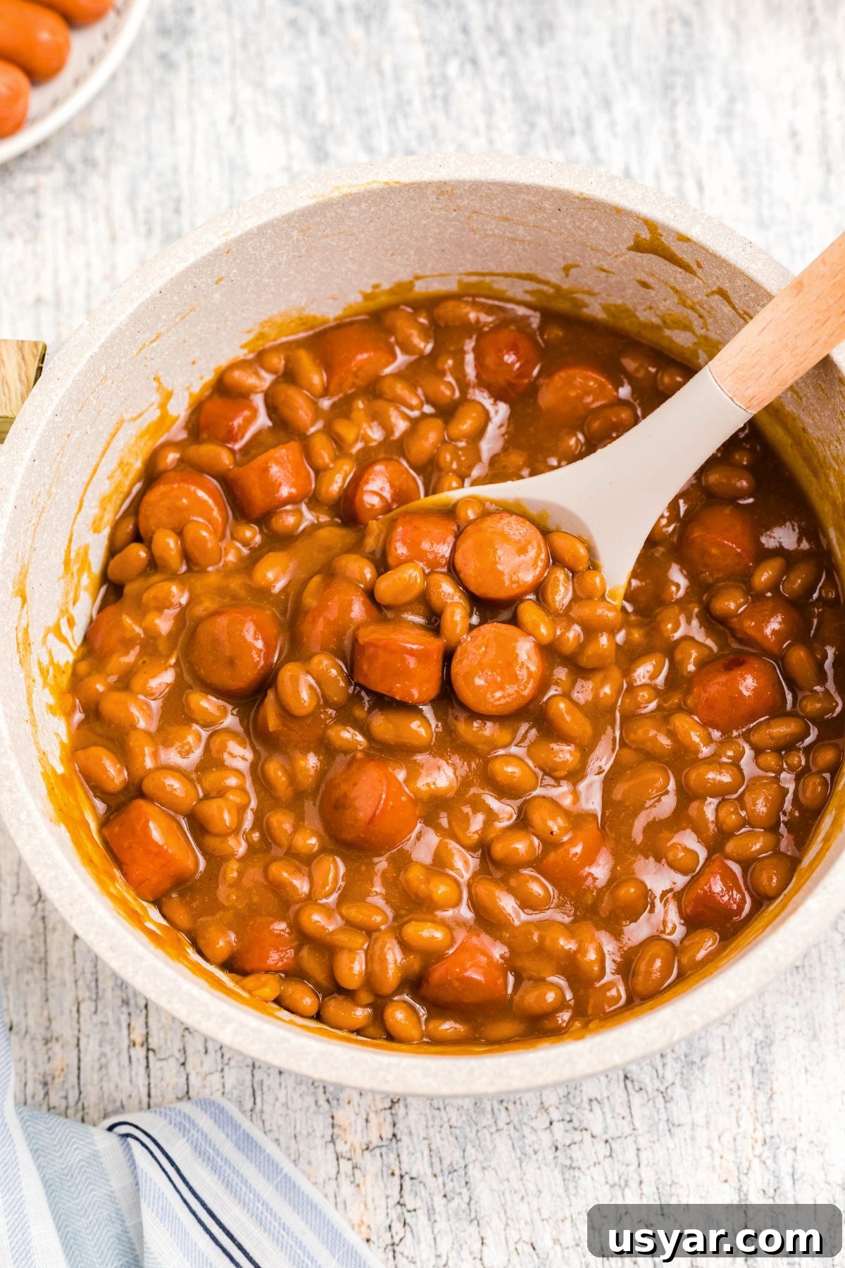 Beanie Weenies Recipe: Classic Hot Dogs in Baked Beans 2 Juicy Beanie Weenies being scooped up out of a large saucepan.