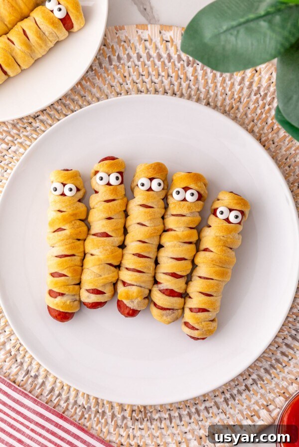 Mummy hot dogs on a white plate, with candy eyes.