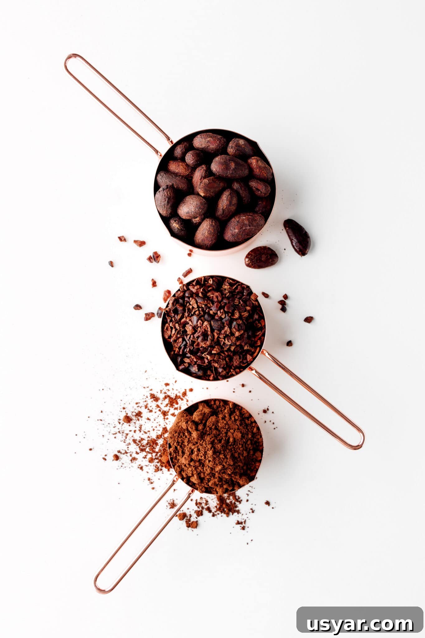 Low-Carb Dessert Baking Tips and Tricks for Perfect Results 3 Three measuring cups with cocoa powder, cocoa nibs and cocoa beans on a bright white tabletop.