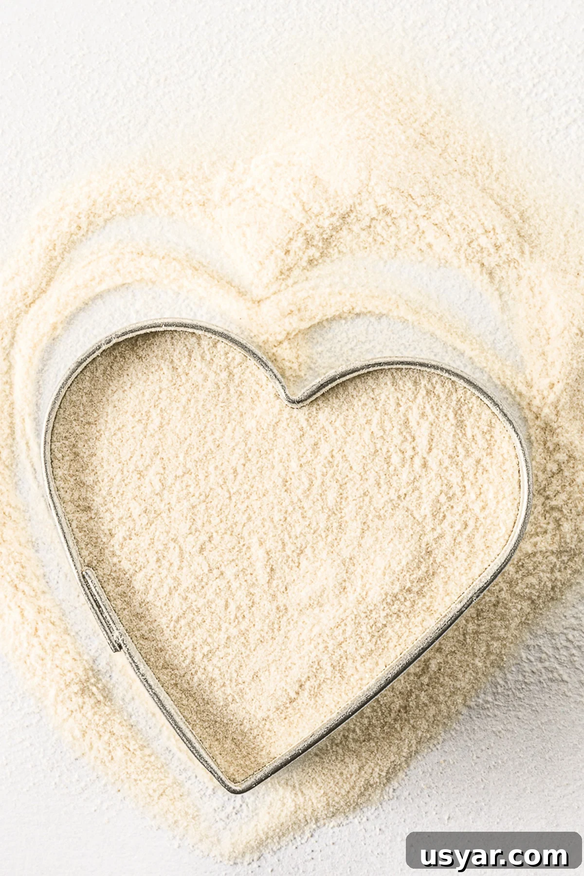 Low-Carb Dessert Baking Tips and Tricks for Perfect Results 6 Xanthan gum poured in an around a heart shaped cookie cutter on a bright white background.