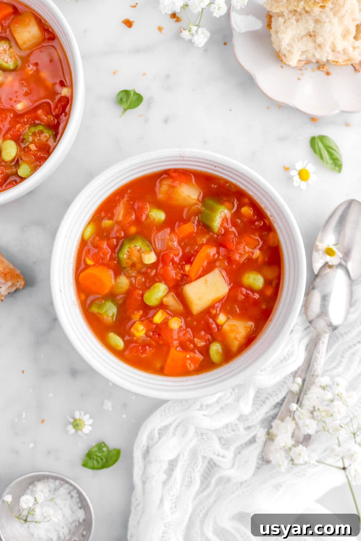 One-Pot Gluten-Free Vegan Vegetable Soup Recipe 7 close up of bowl of vegetable soup with another bowl and two spoons beside, and flowers around.