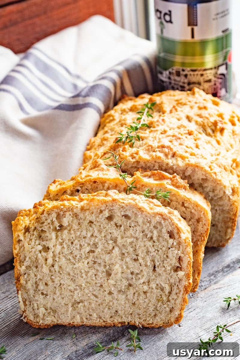 Crusty Herbed Beer Bread Recipe with Garlic and Thyme 2 close up image of sliced Herbed Beer Bread with tea towel and beer can in the background.