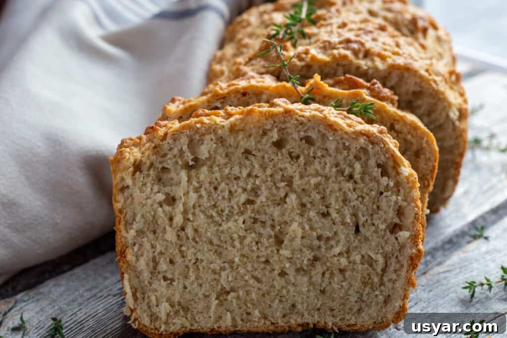 Crusty Herbed Beer Bread Recipe with Garlic and Thyme 3 A loaf of fresh beer bread sitting on a wooden board with thyme and a tea towel.