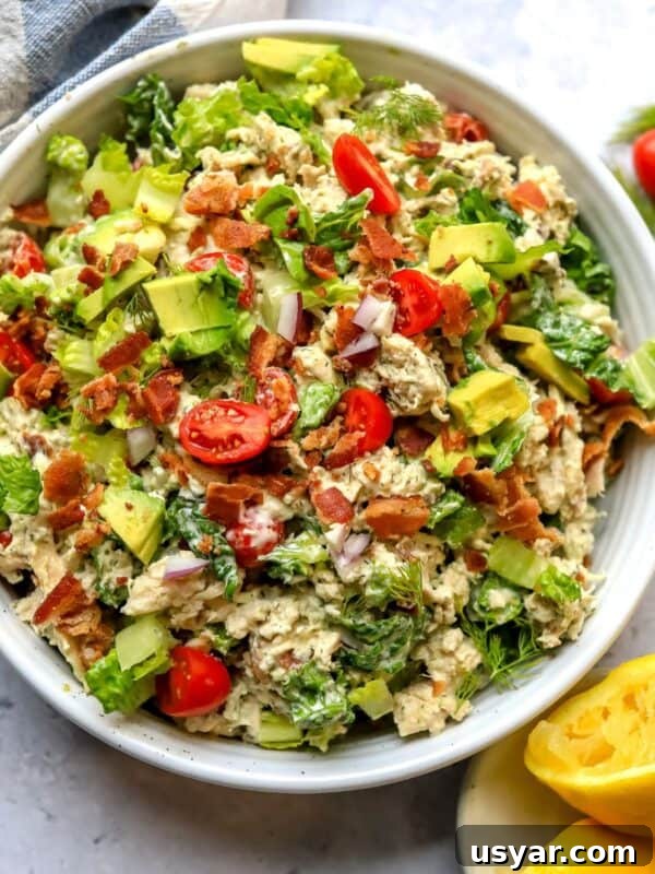 BLT Chicken Salad in a white ceramic bowl with tomatoes and bacon on top.