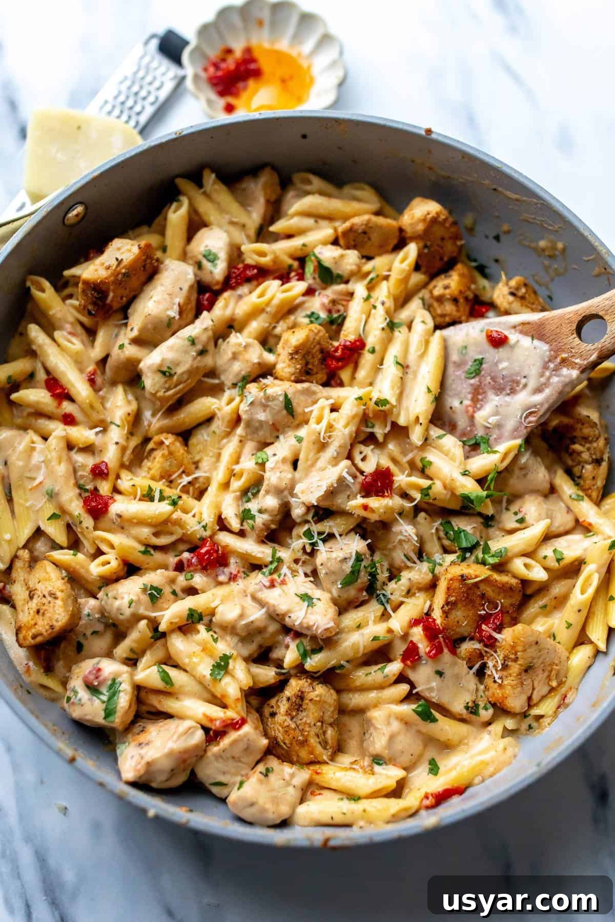 Grey skillet with marry me chicken pasta in it and a wooden spatula in the skillet.