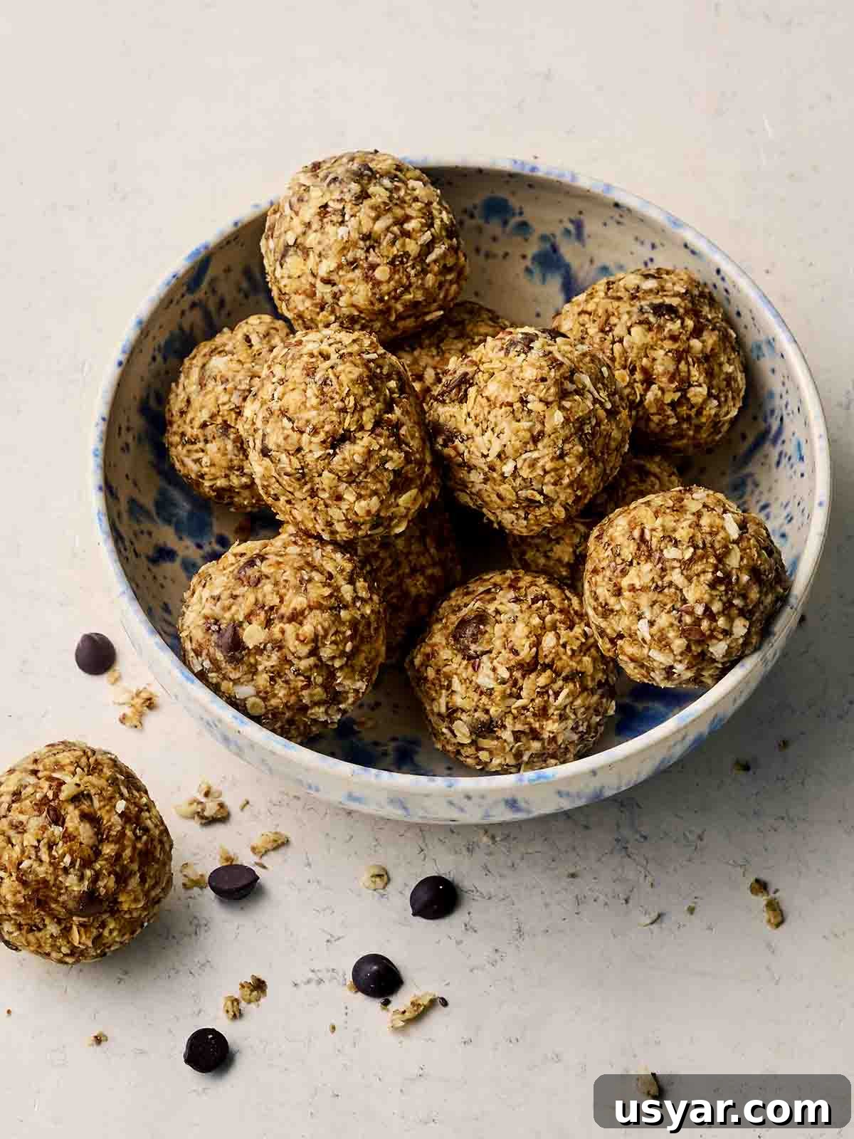 No-Bake Peanut Butter Oat Energy Balls Recipe 2 A bowl of round homemade energy balls, with one on a surface with chocolate chips.