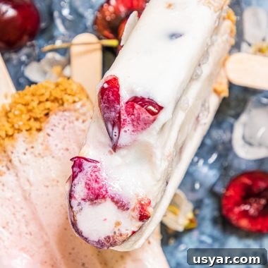 a cherry cheesecake popsicle shown with a bite removed to reveal the sweet dark cherries studding the inside