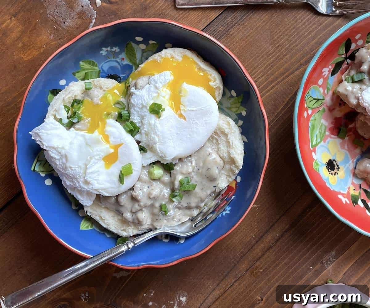 Classic Southern Sausage Gravy Recipe 2 A blue bowl with two biscuits topped with sausage gravy and two poached eggs.