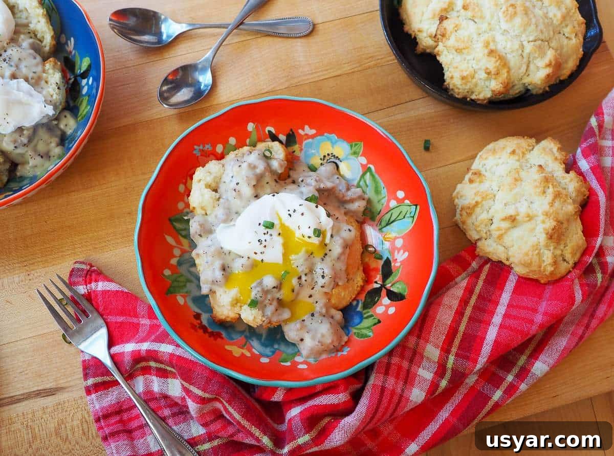 Classic Southern Sausage Gravy Recipe 11 A red bowl of biscuits and gravy topped with a poached egg and a biscuit on the side.