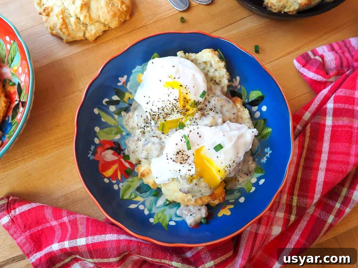 Classic Southern Sausage Gravy Recipe 12 A blue bowl with two biscuits topped with sausage gravy and two poached eggs.