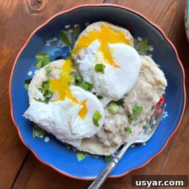 Classic Southern Sausage Gravy Recipe 13 A blue bowl with two biscuits topped with sausage gravy and two poached eggs.