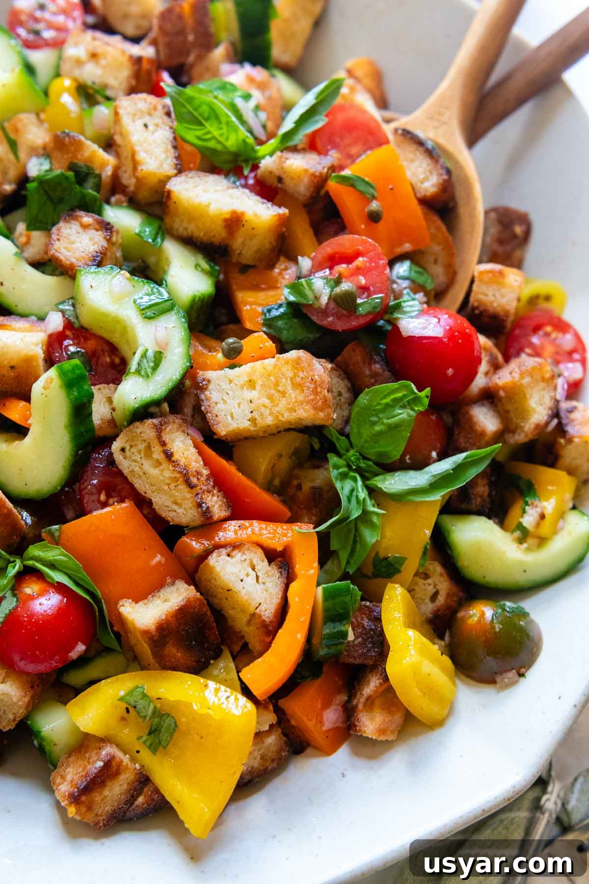 close up of panzanella on a white serving platter with utensils on the side.
