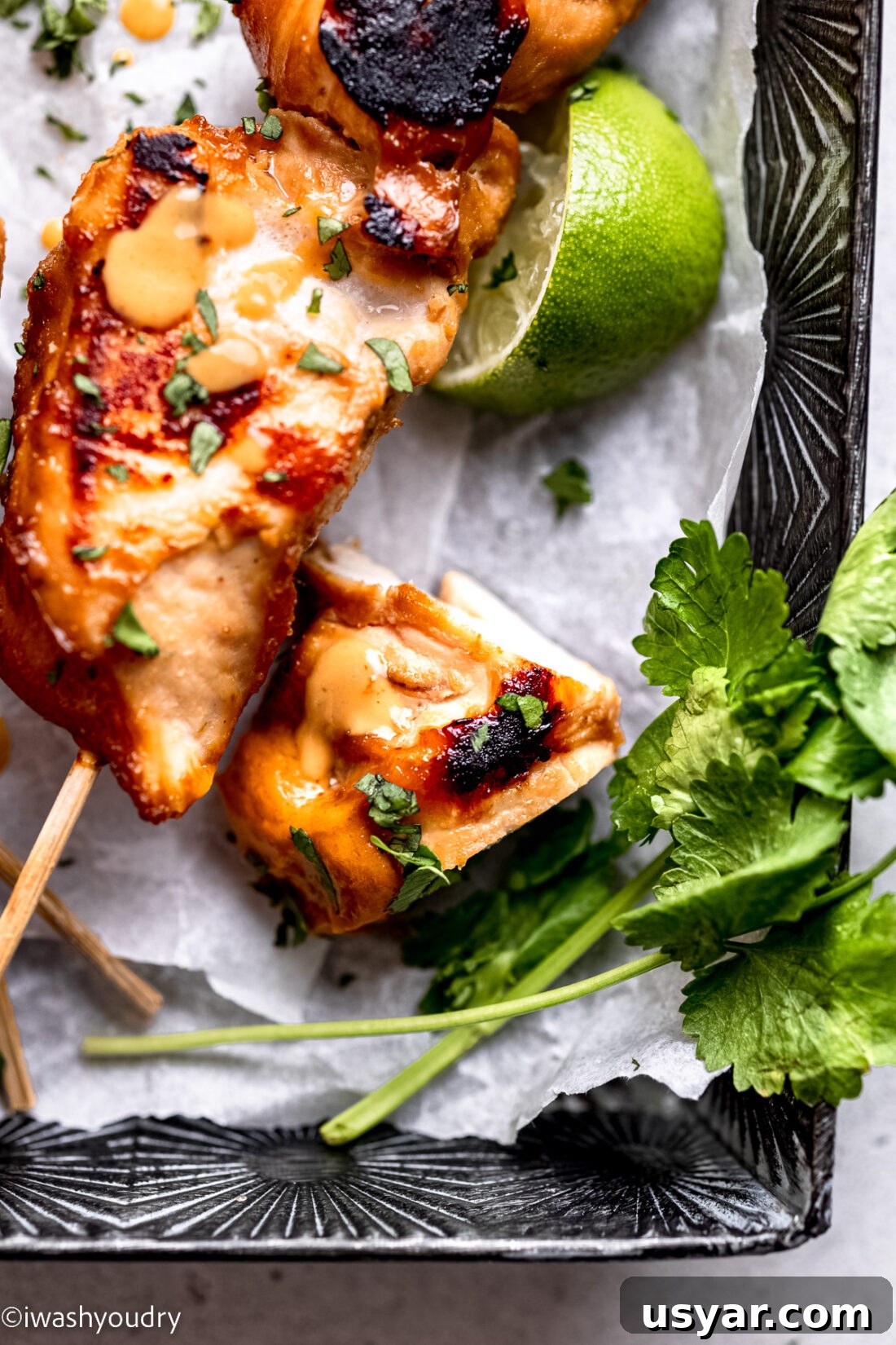 Thai Chicken Satay Recipe with Peanut Dipping Sauce 10 Piece of cooked Thai chicken satay in metal pan with cilantro and lime slice.