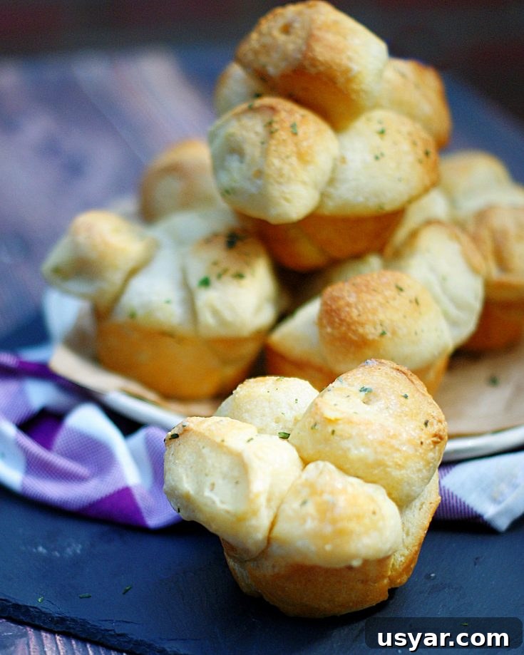 A close up of a shortcut pull apart roll with a plate full of buttery rolls behind it.