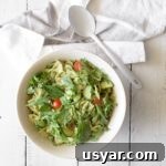Creamy Avocado Pesto Pasta Salad Recipe 3 Creamy avocado pesto pasta salad in a white bowl with a spoon on a white wood table