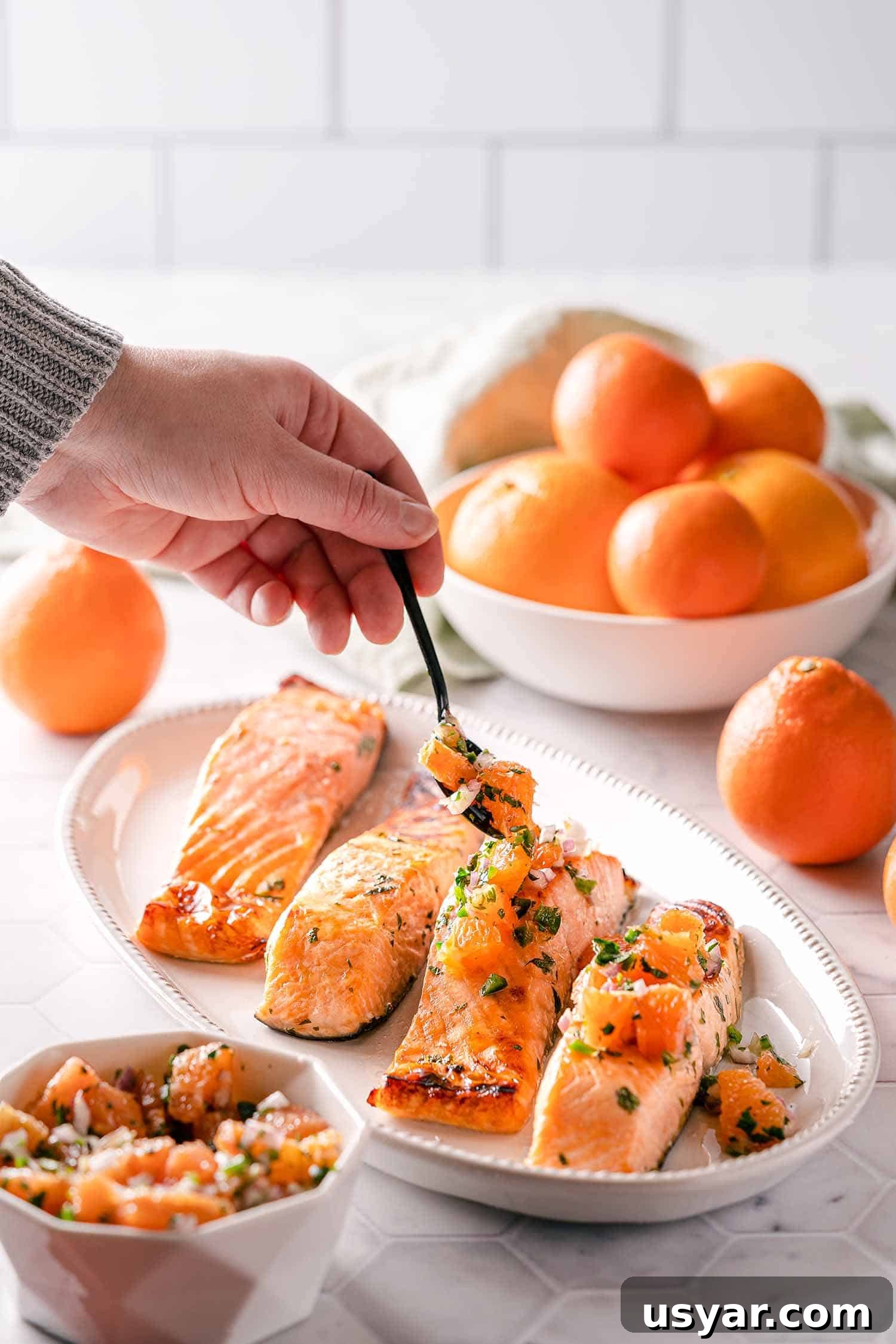 Citrus Herb Salmon with Orange and Red Onion Salsa 10 hand spooning orange salsa over broiled salmon on platter