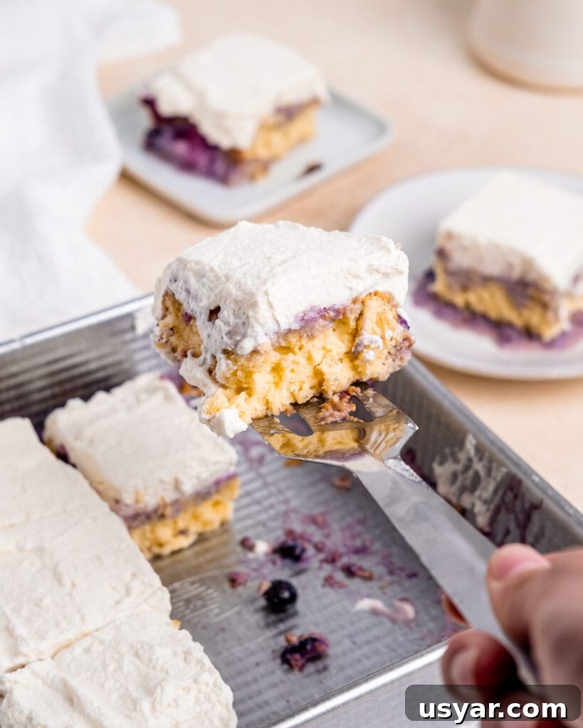 Creamy Milk and Berry Layer Cake 8 Lifting a slice of cake out of the 8x8 inch cake pan with a serving spatula