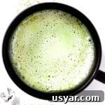 Overhead view of a frothy oat milk matcha latte in a black mug.