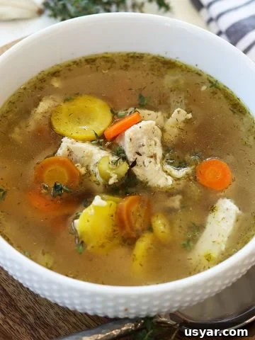 A white bowl full of instant pot chicken soup garnished with fresh herbs.