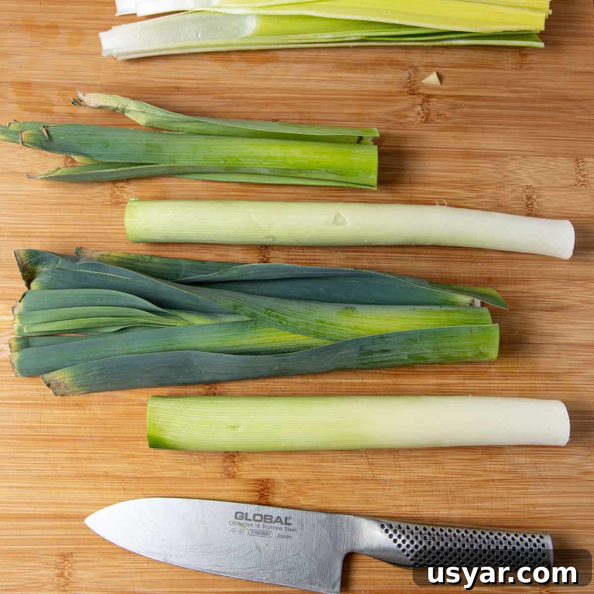 Creamy Vegan Leek and Potato Soup Vichyssoise 4 Photo of 3 leeks on a chopping board with the dark green ends chopped off and lying separately to the white and pale green sections.