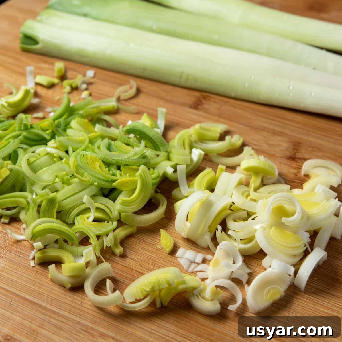 Creamy Vegan Leek and Potato Soup Vichyssoise 7 Photo of sliced leeks on a chopping board with two unsliced leeks in the background.