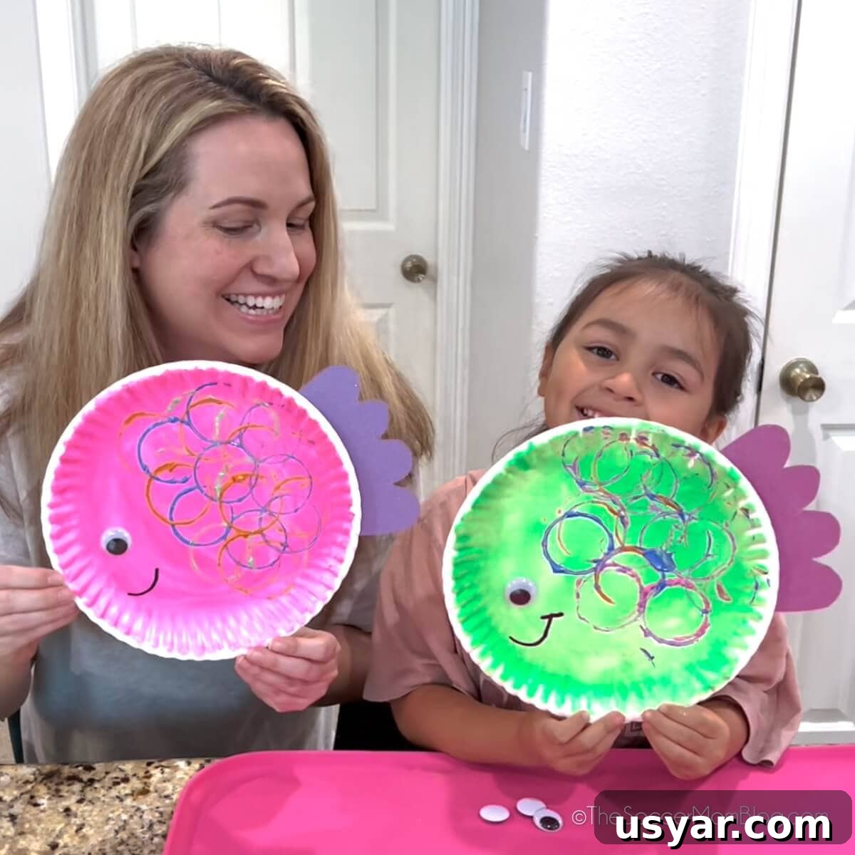 Paper Plate Fish Craft for Kids 5 mom and daughter holding up fish craft made from paper plates.
