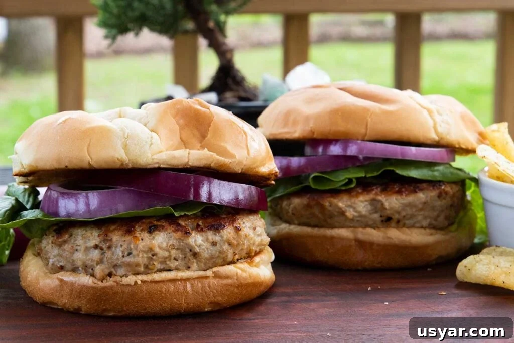 Carolina-Style Grilled Chicken Burger Recipe 23 Two turkey burgers with lettuce and red onion on a cutting board.