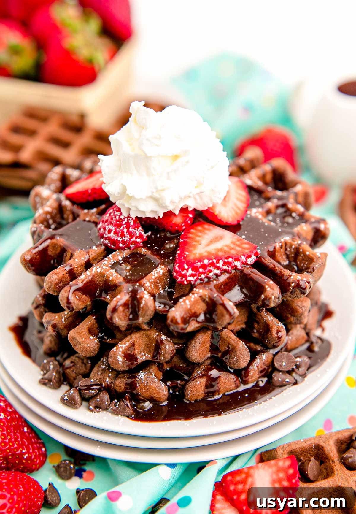From-Scratch Chocolate Waffles Recipe 2 Close up photo of a stack of chocolate waffles topped with chocolate syrup, strawberries, and whipped cream.