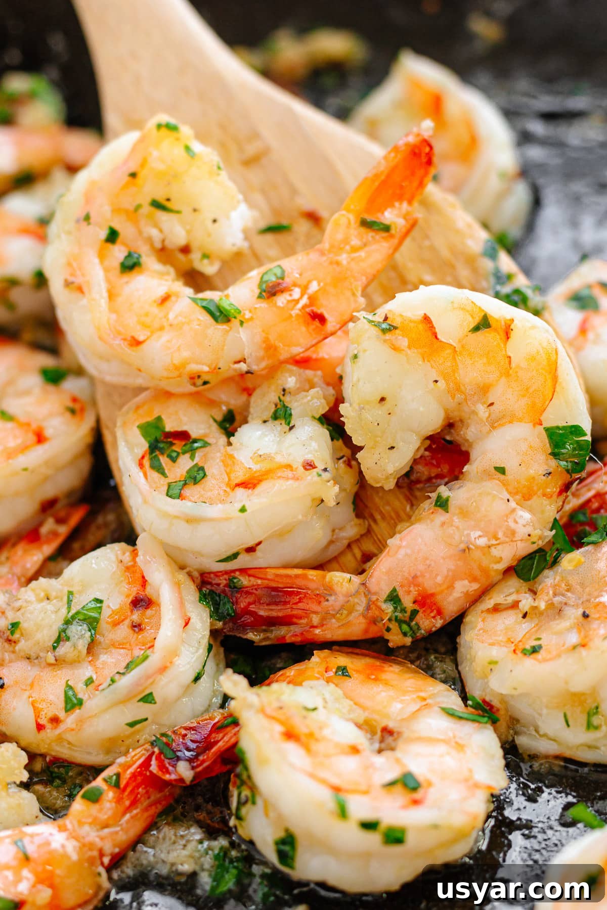 Pan fried shrimp in a cast iron skillet being picked up with a wooden spatula.