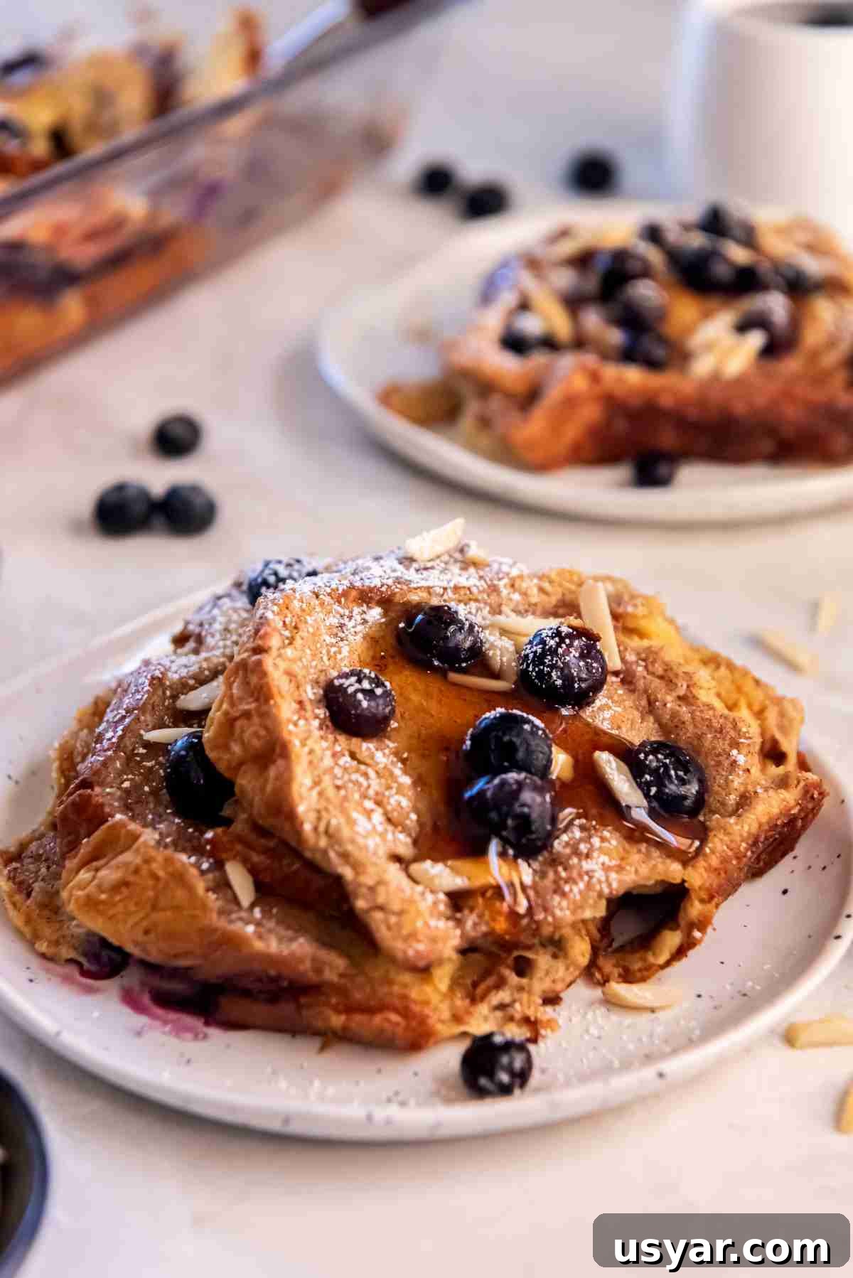 Slice of blueberry brioche French toast bake topped with blueberries, powdered sugar, and maple syrup