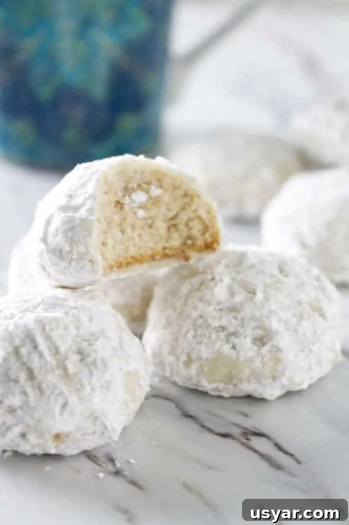 Mexican Snowball Cookies Recipe (Polvorones) 2 A partially eaten cookie on a stack of more snowball cookies.