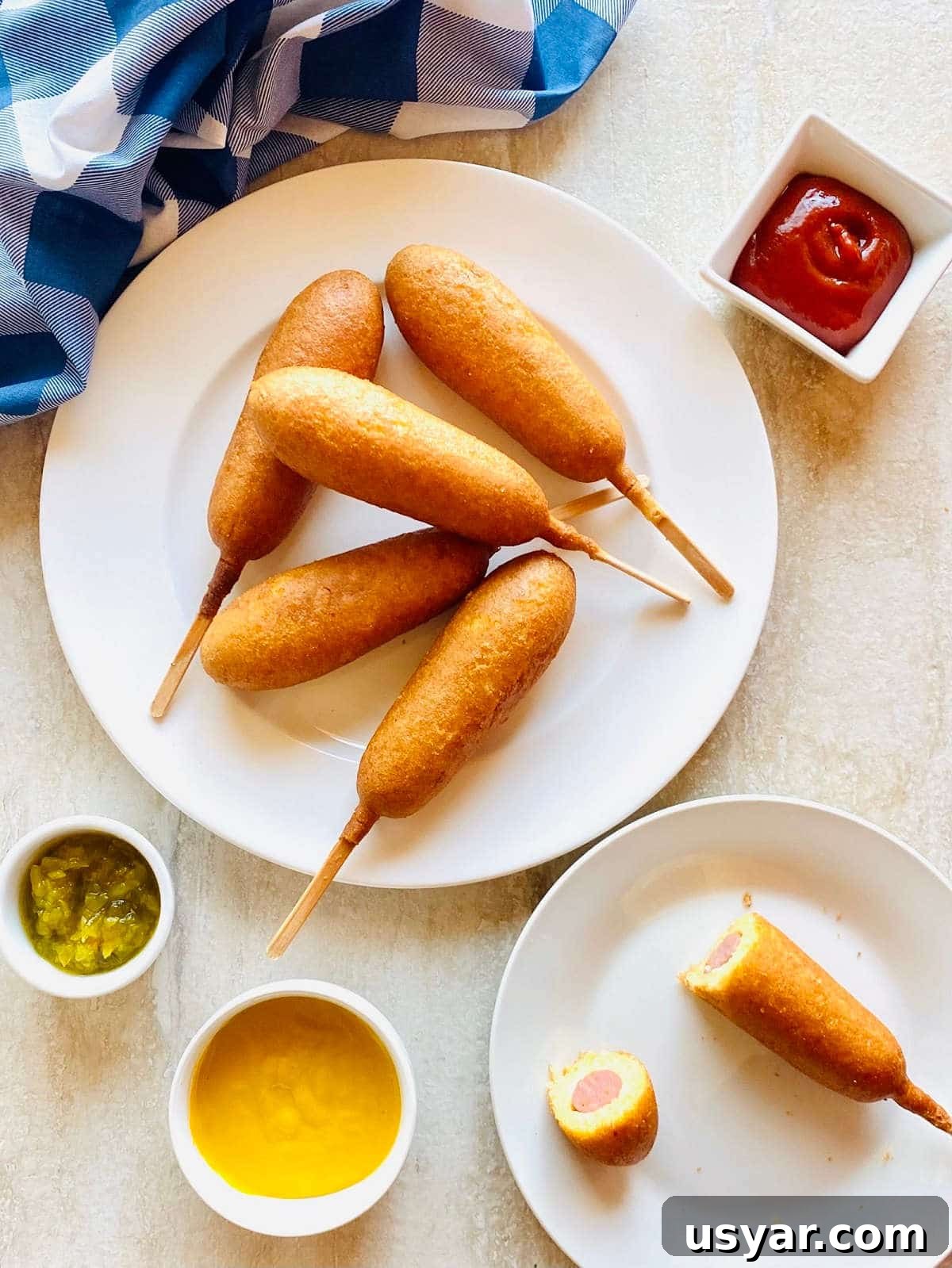 Crispy Air Fryer Corn Dogs Recipe 2 air fryer corn dogs on a plate next to ketchup, mustard and relish