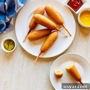 Crispy Air Fryer Corn Dogs Recipe 7 frozen air fryer corn dogs on a plate next to ketchup, mustard and relish