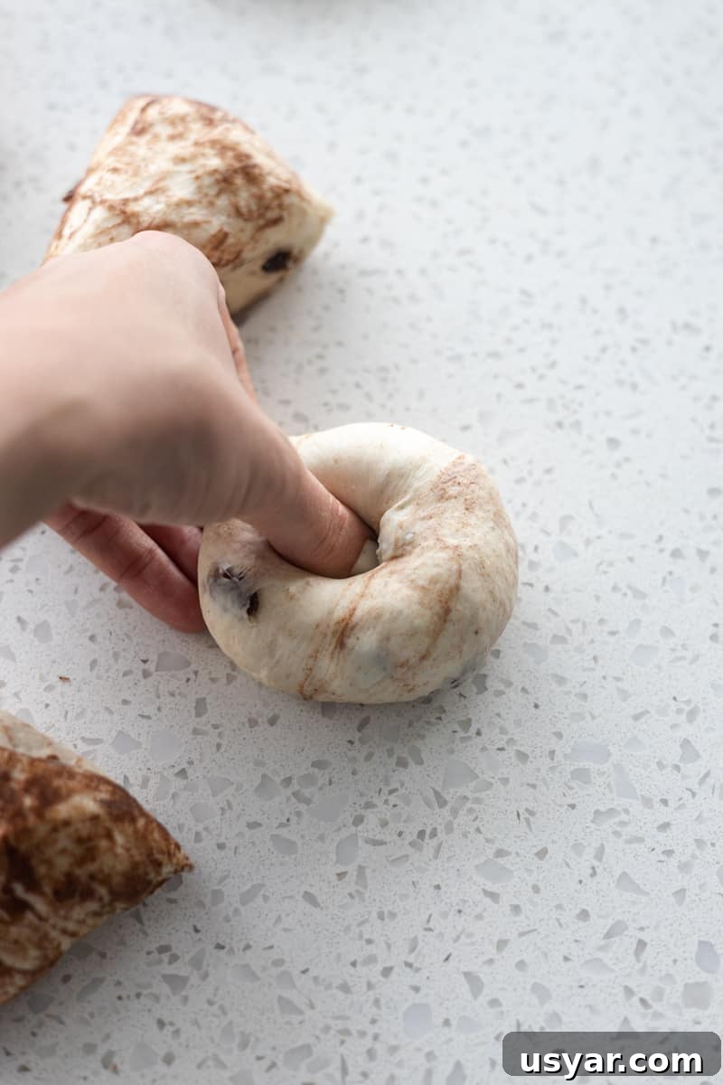 Cinnamon Raisin Sourdough Discard Bagels 8 A hand pressing a hole into the center of the Sourdough Discard Cinnamon Raisin bagels.