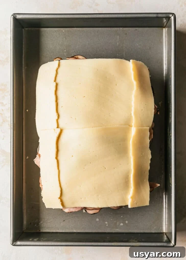 Oven Baked Brown Sugar Ham and Cheese Sliders 6 Hawaiian rolls layered with ham and havarti in a silver pan.