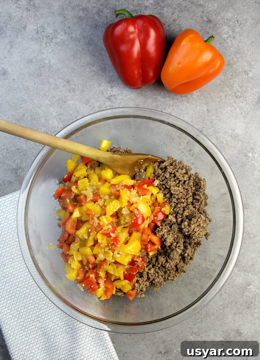 A clear glass bowl filled with cooked ground beef and chopped peppers for unstuffed pepper casserole.
