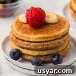High Protein Cottage Cheese Blender Pancakes 11 Close up of four protein pancakes stacked and topped with berries and bananas and syrup.