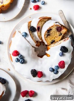 tabletop with a mixed berry pound cake topped with icing and a few slices cut.