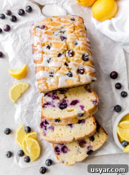 lemon blueberry bread with three slices cut off the end on top of parchment paper with fresh blueberries and lemon slices