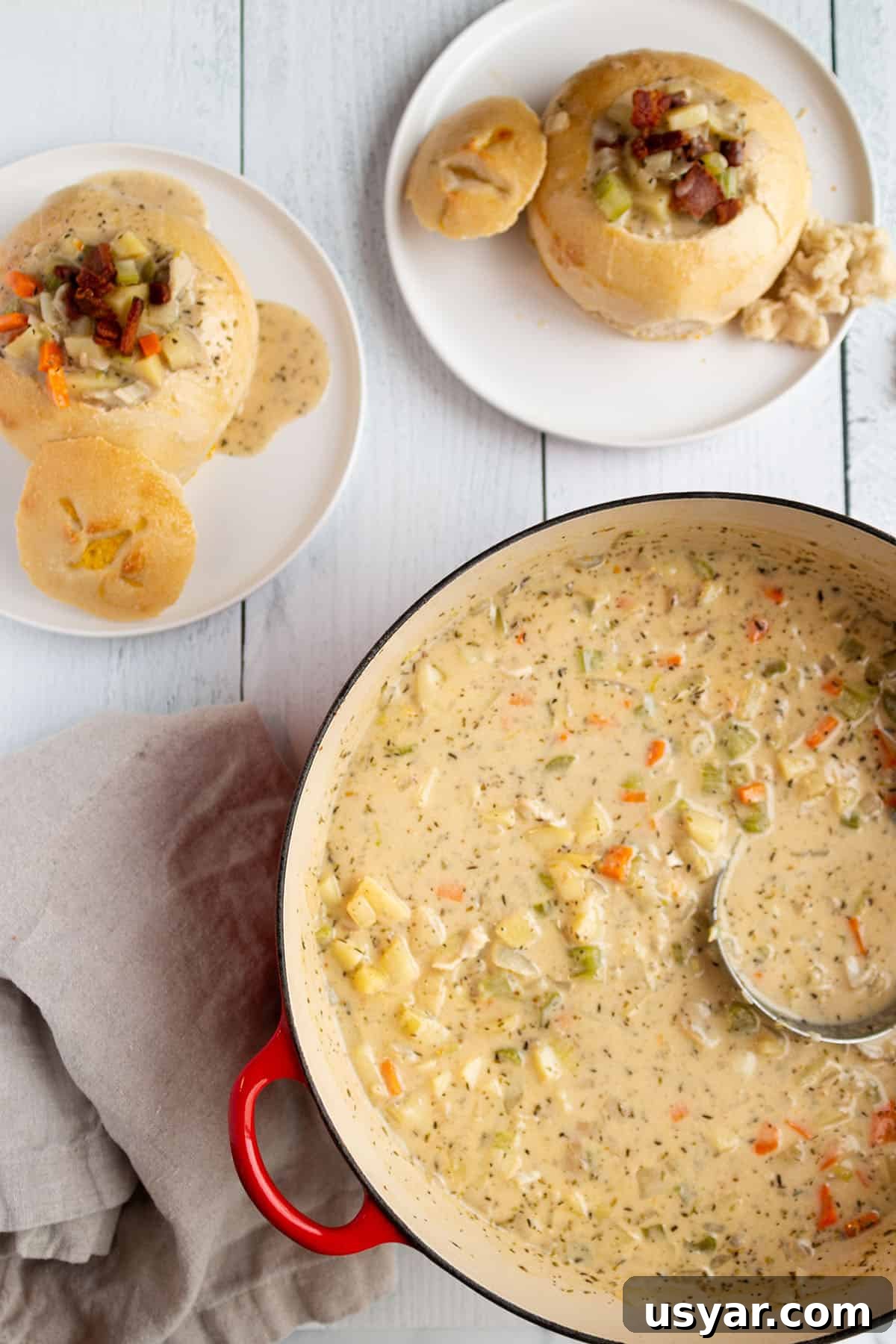 Creamy Razor Clam Chowder Recipe 2 A large soup pot with a creamy clam chowder and two plates with sourdough bread bowls.