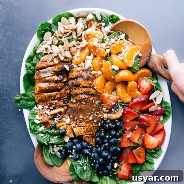 Chicken spinach salad on a large platter, elegantly dressed and garnished with fresh fruit and nuts.
