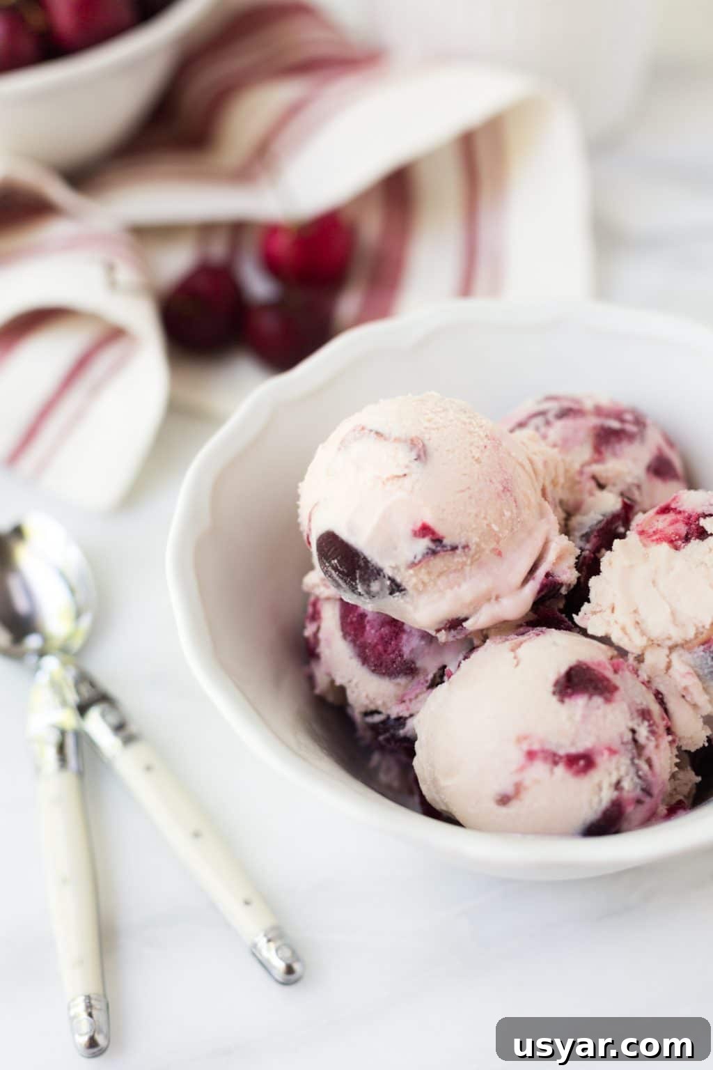 scoops of rum cherry ice cream in a white bowl next to spoons and a red and white striped napkin