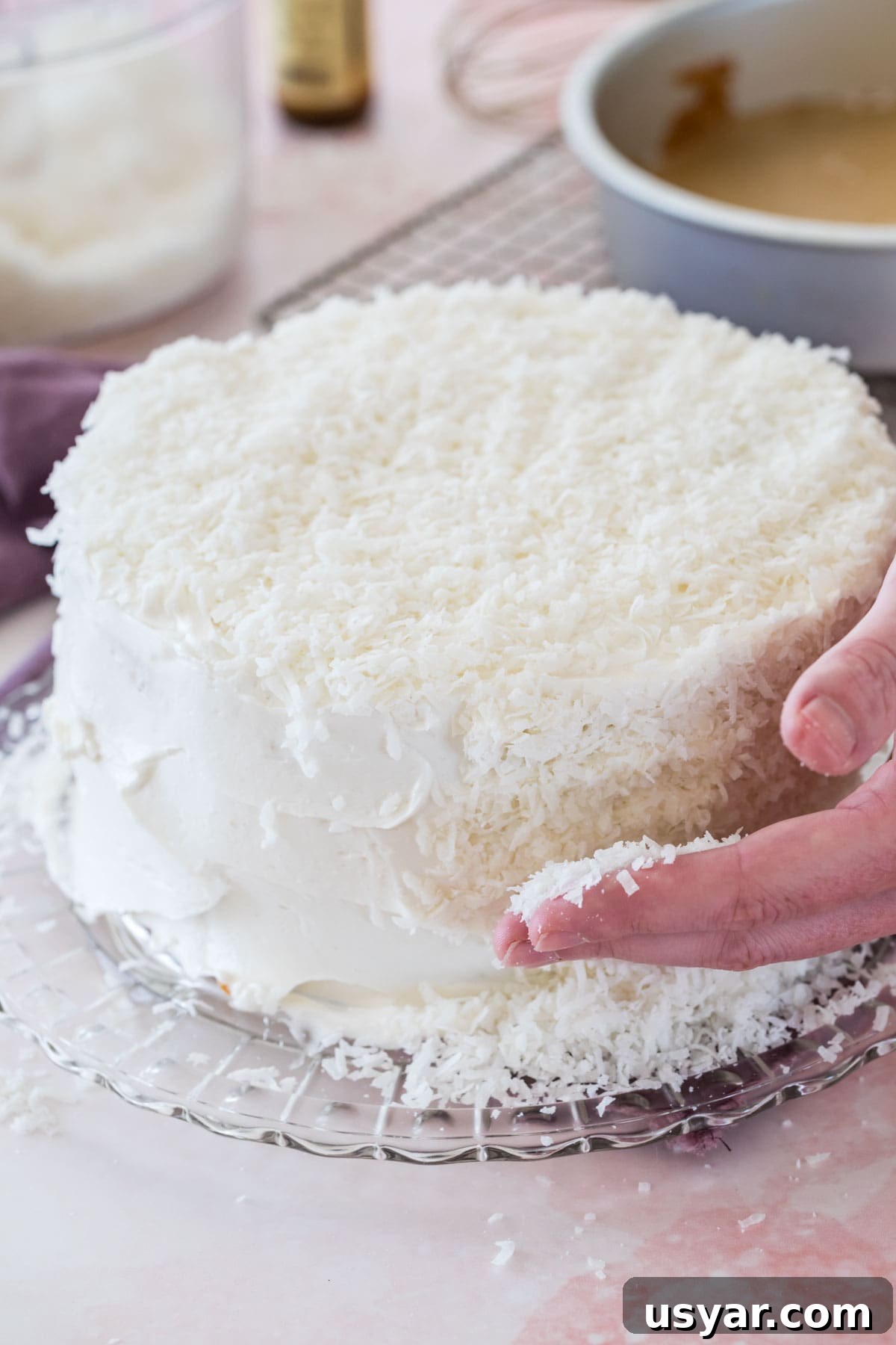 Classic Coconut Cake Recipe with Coconut Cream Frosting 7 Covering a white-iced cake with shredded coconut